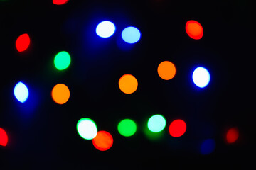 Multicolored lights out of focus on a black background, festive bokeh, abstract colored backdrop