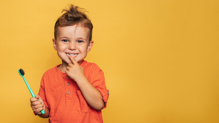 Happy baby toddler boy brushing his teeth with a toothbrush on a yellow background. Health care, oral hygiene. A place for your text.