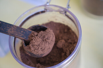 Cocoa powder in a spoon scooped out of a plastic jar.