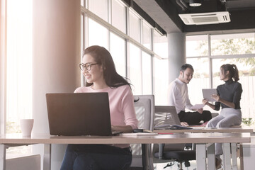Asian business woman who sitting work by notebook at the office with daylight from window and blur garden background.