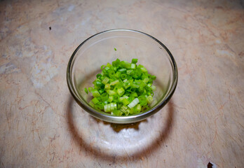 finely cut green onions in a glass bowl on a light pink table