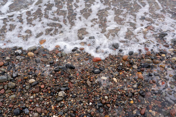 Water is washed up on a stony sandy beach, texture background wallpaper, stones and sand