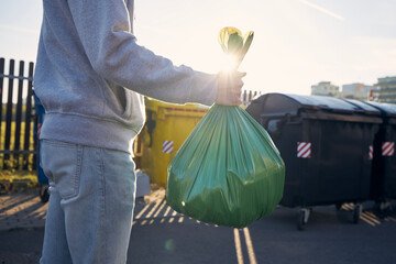 Man walking with rubbish. Hand carrying plastic bag against garbage cans on street..