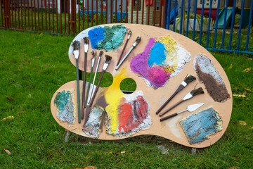 Wooden palette with paints and brushes on a background of green grass on a clear sunny day....