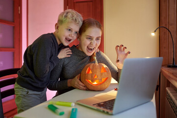Online distance communication. Happy Brother and Sister having video chat on laptop with friends or grandparents celebrating Halloween
