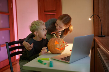 Online distance communication. Happy Brother and Sister having video chat on laptop with friends or grandparents celebrating Halloween