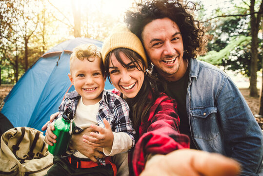 Happy family camping in the forest taking selfie portrait together - Mother, father and son having fun trekking in the nature sitting in front of the tent - Family, nature and trekking concept