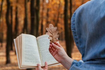 Man in hood holds open book and oak leaf..