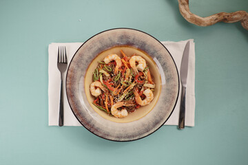 Stir fry noodles with vegetables and shrimps in pan. Slate background. Top view.
