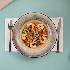 Stir fry noodles with vegetables and shrimps in pan. Slate background. Top view.