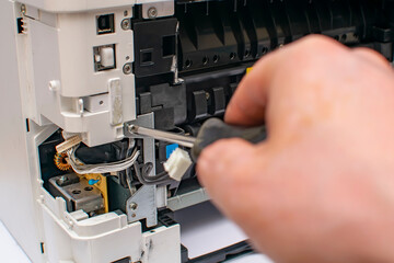 close up, a view of the tip of a phillips screwdriver, with which the master hand unscrews the bolt of the disassembled printer thermoblock, fuser