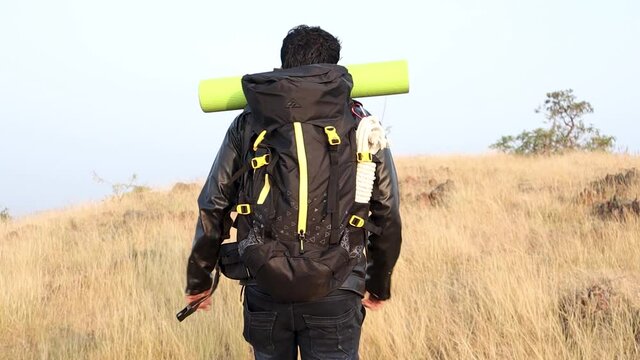 Back view of traveler or hiker climbing the hill with rucksack by holding stick for support - concept of wanderer and leisure activities