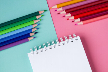 Colored pencils and notepad on a blue and pink background