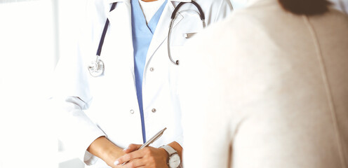 Unknown woman-doctor and patient in hospital. Blonde physician controls medication history records and exam results while using clipboard, close-up. Medicine concept