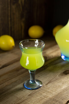 Limoncello liqueur or poncha drink in vintage glass on a wooden table with lemons and decanter with lemoncello