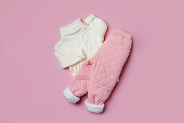White sweater and warm  pants on pink background. Stylish childrens outerwear. Winter fashion outfit