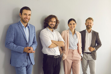 Group portrait of four successful young business people. Team of 4 happy confident businesspeople in smart office wear posing together against grey studio background