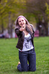 Young blonde with blue eyes in the park on green grass flirts with the camera