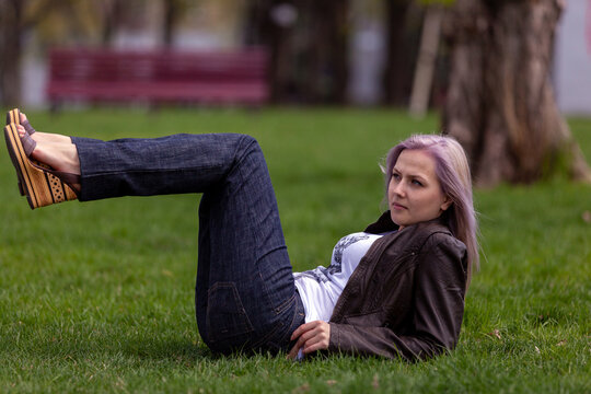 Young blonde with blue eyes in the park on green grass flirts with the camera