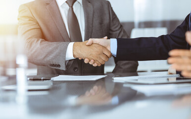 Unknown business people are shaking hands after contract signing in modern office, close-up. Handshake as successful negotiation ending