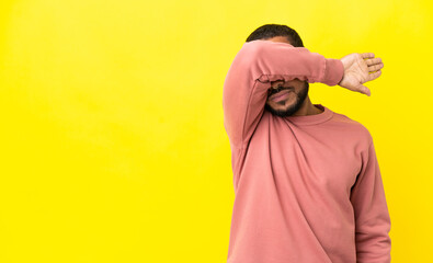 Young latin man isolated on yellow background covering eyes by hands