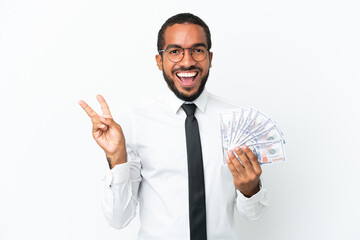 Young business latin man taking a lot of money isolated on white background smiling and showing victory sign