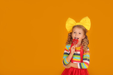a beautiful blonde girl with a yellow bow in a red skirt, a colored blouse holds a heart-shaped lollipop in her hands