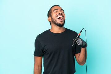 Tattoo artist Ecuadorian man isolated on blue background laughing