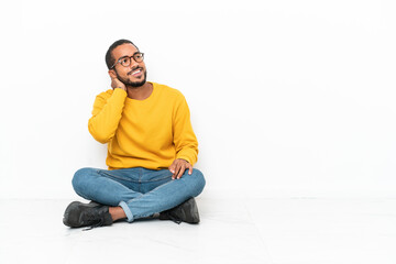 Young Ecuadorian man sitting on the floor isolated on white wall thinking an idea