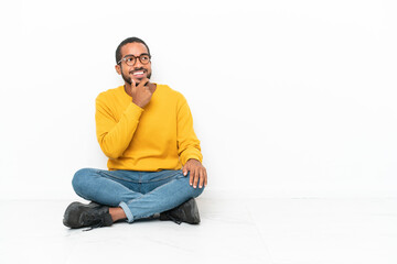 Obraz premium Young Ecuadorian man sitting on the floor isolated on white wall looking to the side
