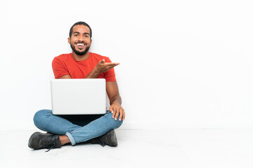 Young Ecuadorian man with a laptop sitting on the floor isolated on white background presenting an idea while looking smiling towards
