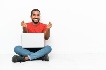 Young Ecuadorian man with a laptop sitting on the floor isolated on white background making money gesture