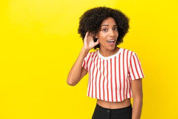 Young African American woman isolated on yellow background listening to something by putting hand on the ear