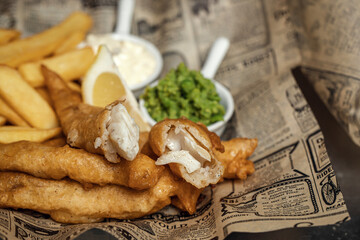 British Traditional crispy Fish and chips with mashed peas, tartar sauce on newspaper