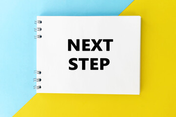 The inscription next step on an open notebook that lies on a colored background.