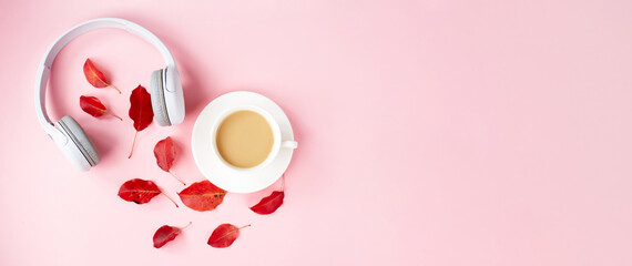 Fall flat lay composition with red autumn leaves, cup of coffee and white headphones on pink background. Autumn podcast background. Autumn playlist concept.