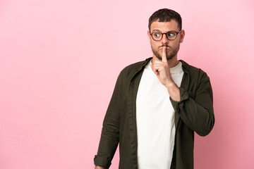 Young Brazilian man isolated on pink background showing a sign of silence gesture putting finger in mouth