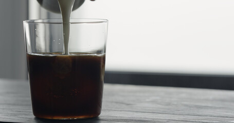pour milk into ice coffee on black wood table