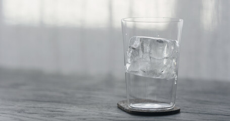 clear ice cube in tumbler glass on black oak table