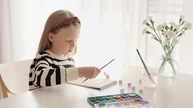 Little kid girl artist drawing coloring picture with paints and brushes. Child hobby creative art activity at home play alone.
