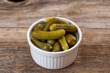 Crunchy pickled cornichons in a white ceramic bowl. Marinated green gherkins. Pickled cucumber. Delicious baby pickles. Tasty canned vegetables