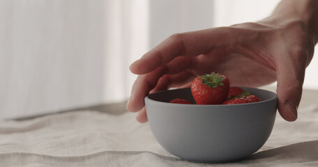 man put fresh strawberries in blue bowl on linen cloth