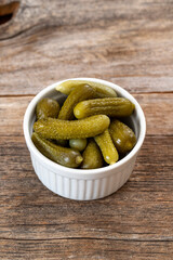 Crunchy pickled cornichons in a white ceramic bowl. Marinated green gherkins. Pickled cucumber. Delicious baby pickles. Tasty canned vegetables