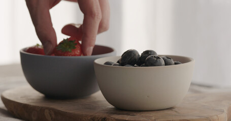 man take fresh strawberries and blueberries in bowls on olive wood board