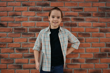 Indoor portrait of Caucasian boy dressed in shirt standing against brick wall holding laptop.