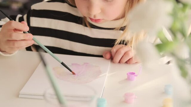 Little kid girl artist drawing coloring picture with paints and brushes. Child hobby creative art activity at home play alone.