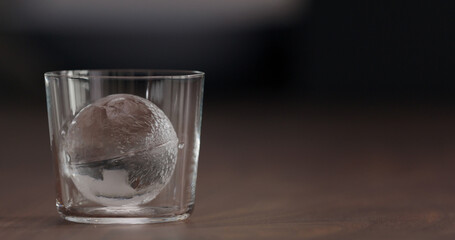 clear ice ball in tumbler glass on black walnut table