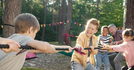 Full length view of the kids at summer camp playing tug or war with their senior teacher at the forest. Happy childhood and activities concept