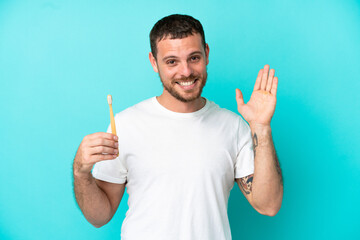 Young Brazilian man brushing teeth isolated on blue background saluting with hand with happy expression