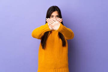 Teenager Brazilian girl over isolated purple background making stop gesture with her hand to stop...
